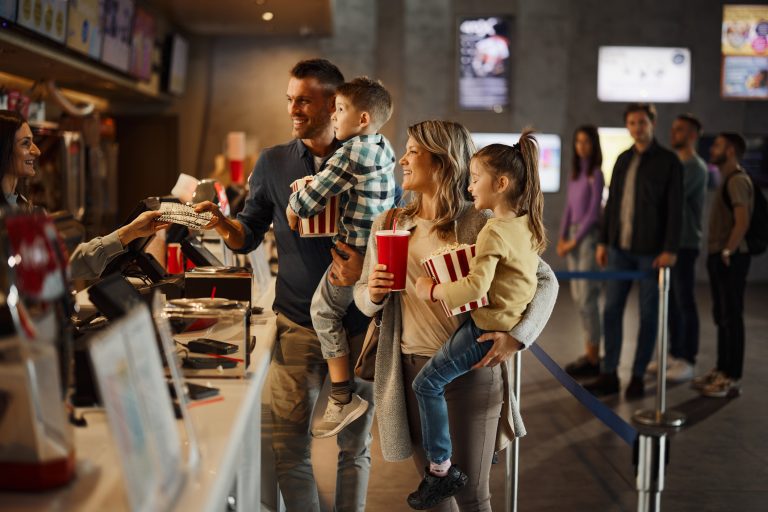 Happy family buying movie tickets in cinema.